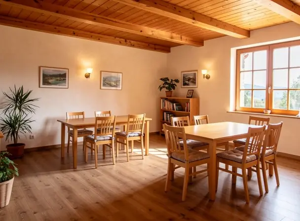 Bright wooden common room inside a countryside guesthouse, simple tables and chairs, large windows with natural daylight, minimal and warm decor, welcoming and calm atmosphere, high resolution interior photography
